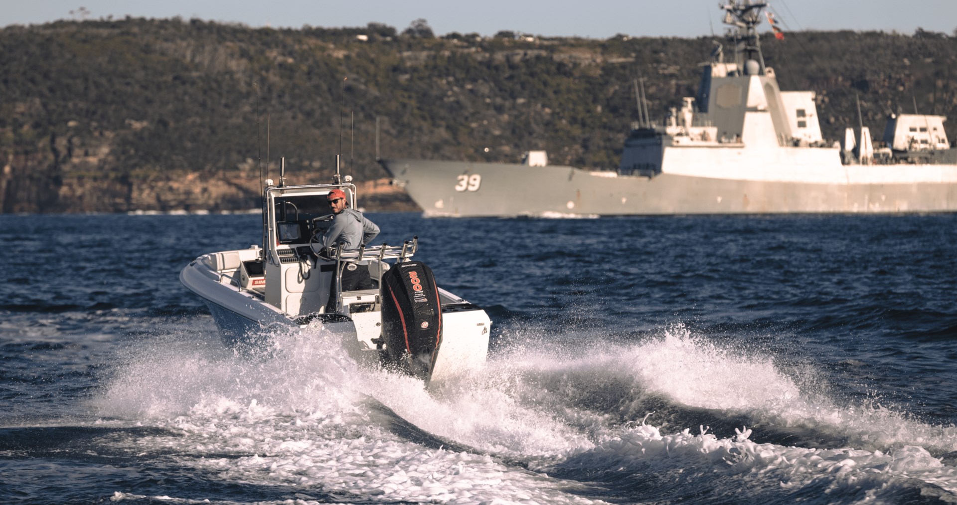 A man driving a center console fishing boat near a navy battle ship